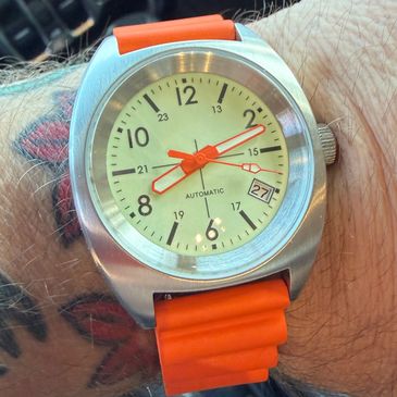 Close-up of a wristwatch with an orange strap on a tattooed arm.