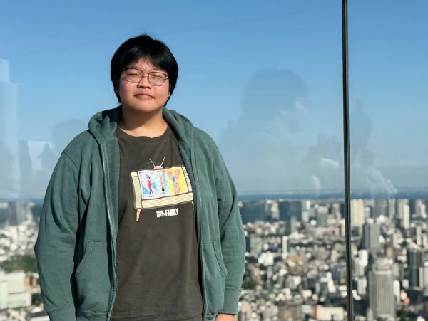 Person standing outdoors with eyes closed, cityscape in the background.