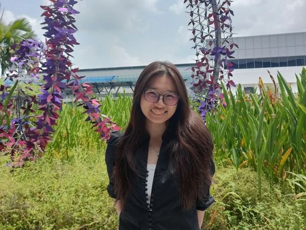 Smiling woman with long hair and glasses outdoors.