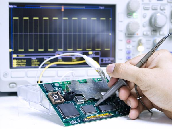 Hand holding a circuit board with another on a table.