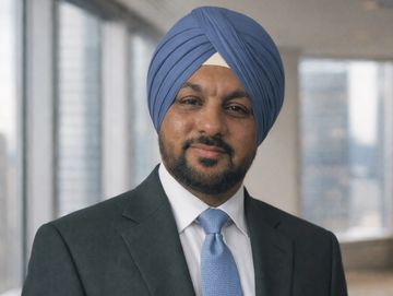 Confident man in a suit and blue turban standing in an office with city views.
