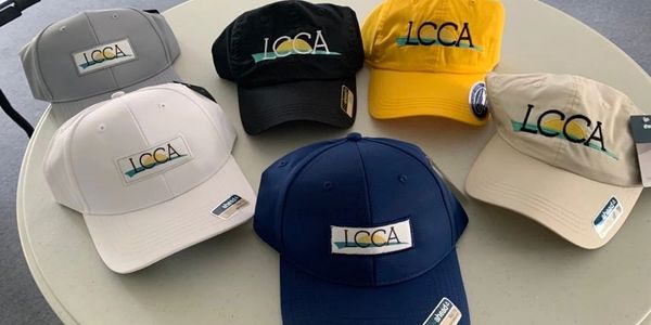 Six LCCA logo caps in various colors displayed on a round table.