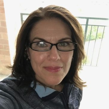 Diane, a middle aged white woman with below-chin length, dark brown hair, wearing black glasses. 