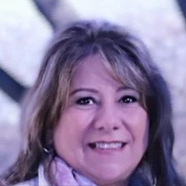 Marcia, a middle aged white woman with brown hair, wearing silver earrings, smiling at the camera.