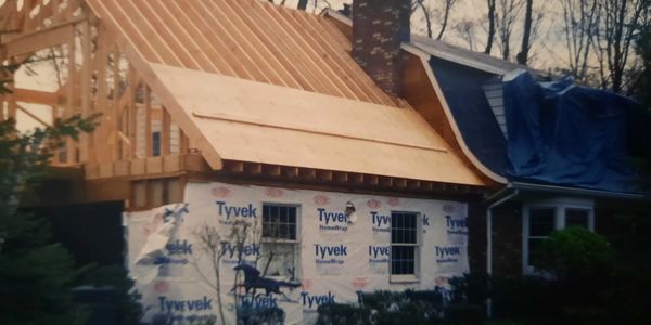 House under construction with new wooden roof framing and Tyvek wrap on walls.