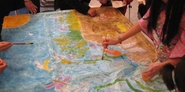 People collaboratively painting a large colorful mural on a table.