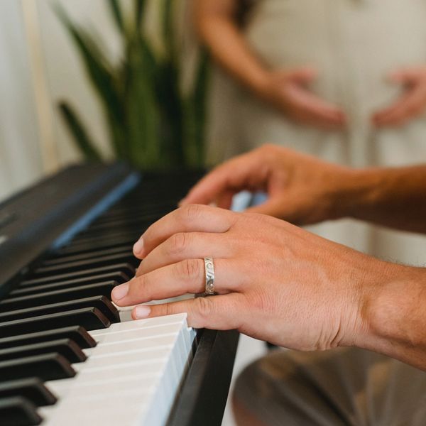 Hands on the piano with a pregnant belly in the background.