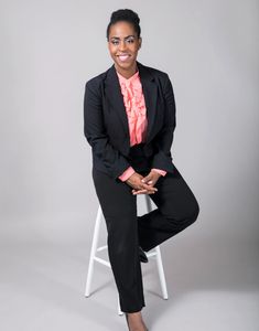 Sonya Harris Speech Language Pathologist smiling in a black suit sitting on a stool