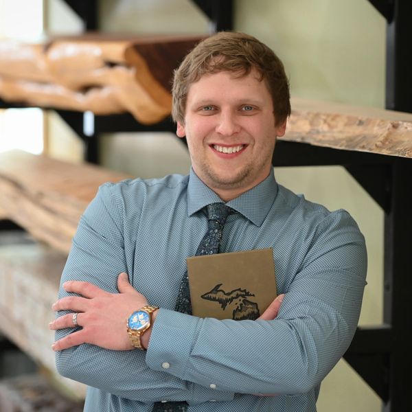 Smiling man in a blue shirt holding a notebook with a Michigan map design.