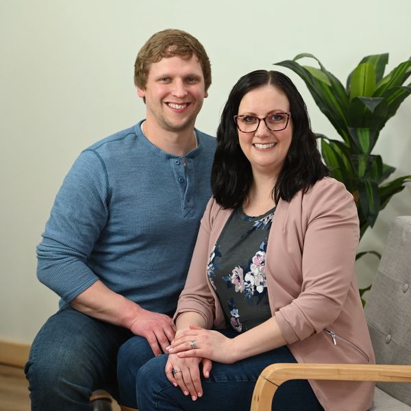 A smiling couple sitting together indoors, holding hands.