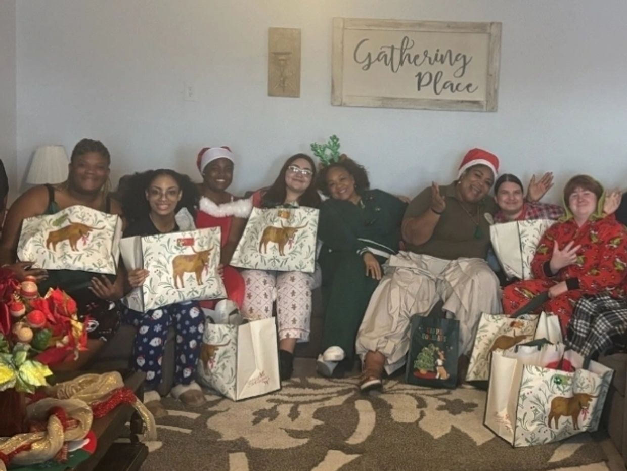 Group of friends in festive attire holding holiday gift bags, sitting together in a cozy room.