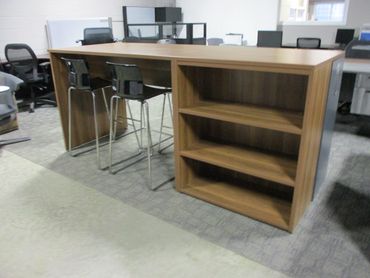 Modern wooden office table with high chairs and open shelves.
