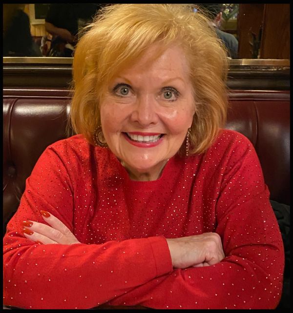 Smiling woman in a red sweater sitting with crossed arms.