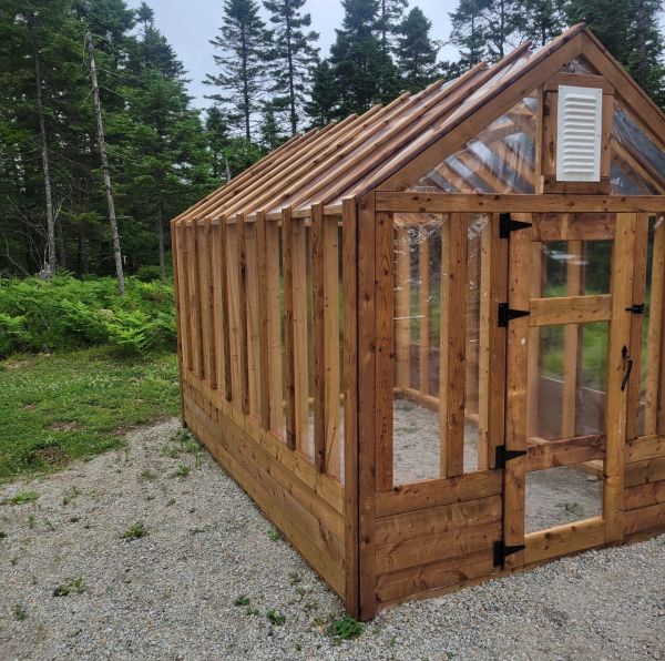 Wooden greenhouse with transparent plastic panels in a forested area.