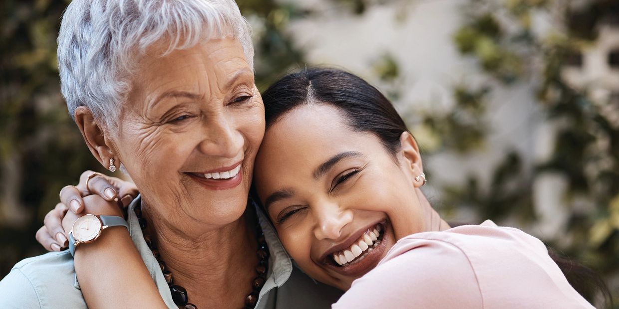 A joyful young woman hugging an elderly woman, both smiling warmly.