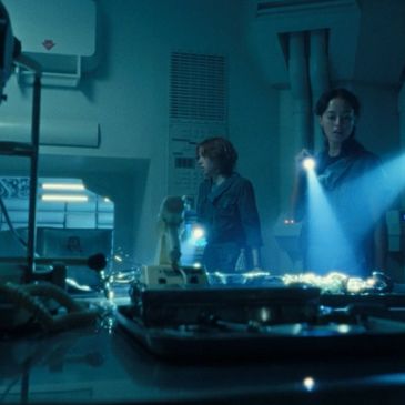 Two people exploring a dimly lit, futuristic lab with flashlights.