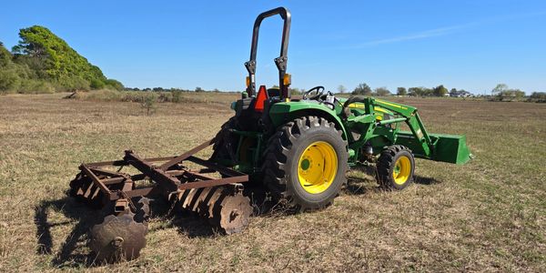 A modern tractor with an old model disc harrow in an open field.