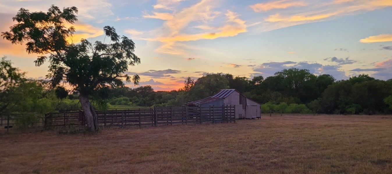 A rustic barn and fenced area at sunset with colorful clouds.