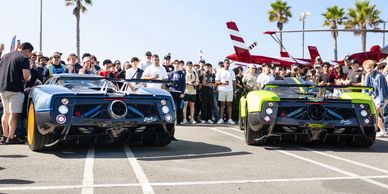 Two exotic sports cars parked with a crowd and palm trees behind them.