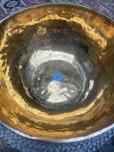 A large, reflective brass or bronze bowl with a blue sticker labeled 'G' inside.