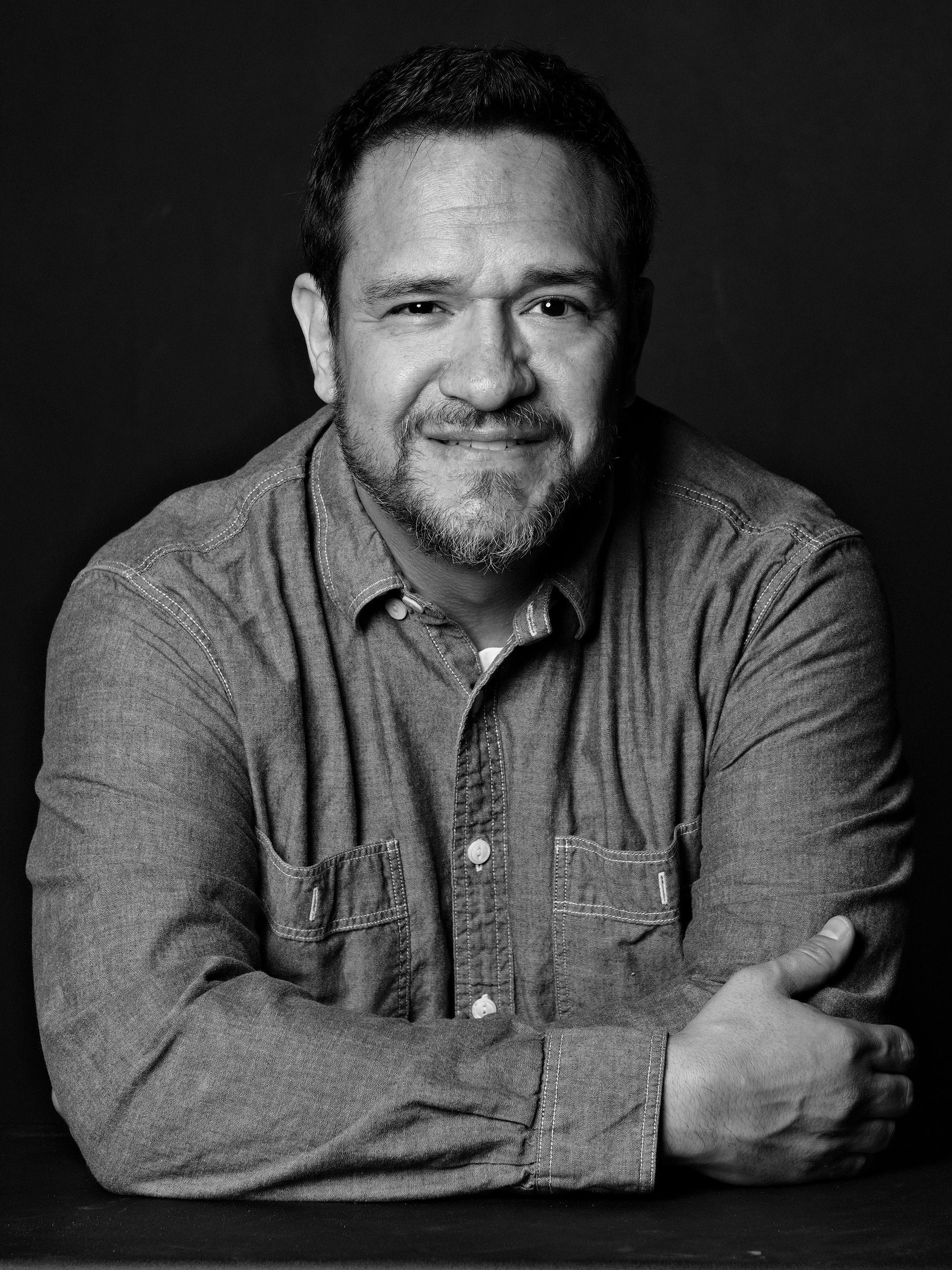 Black and white portrait of a smiling man in a denim shirt.