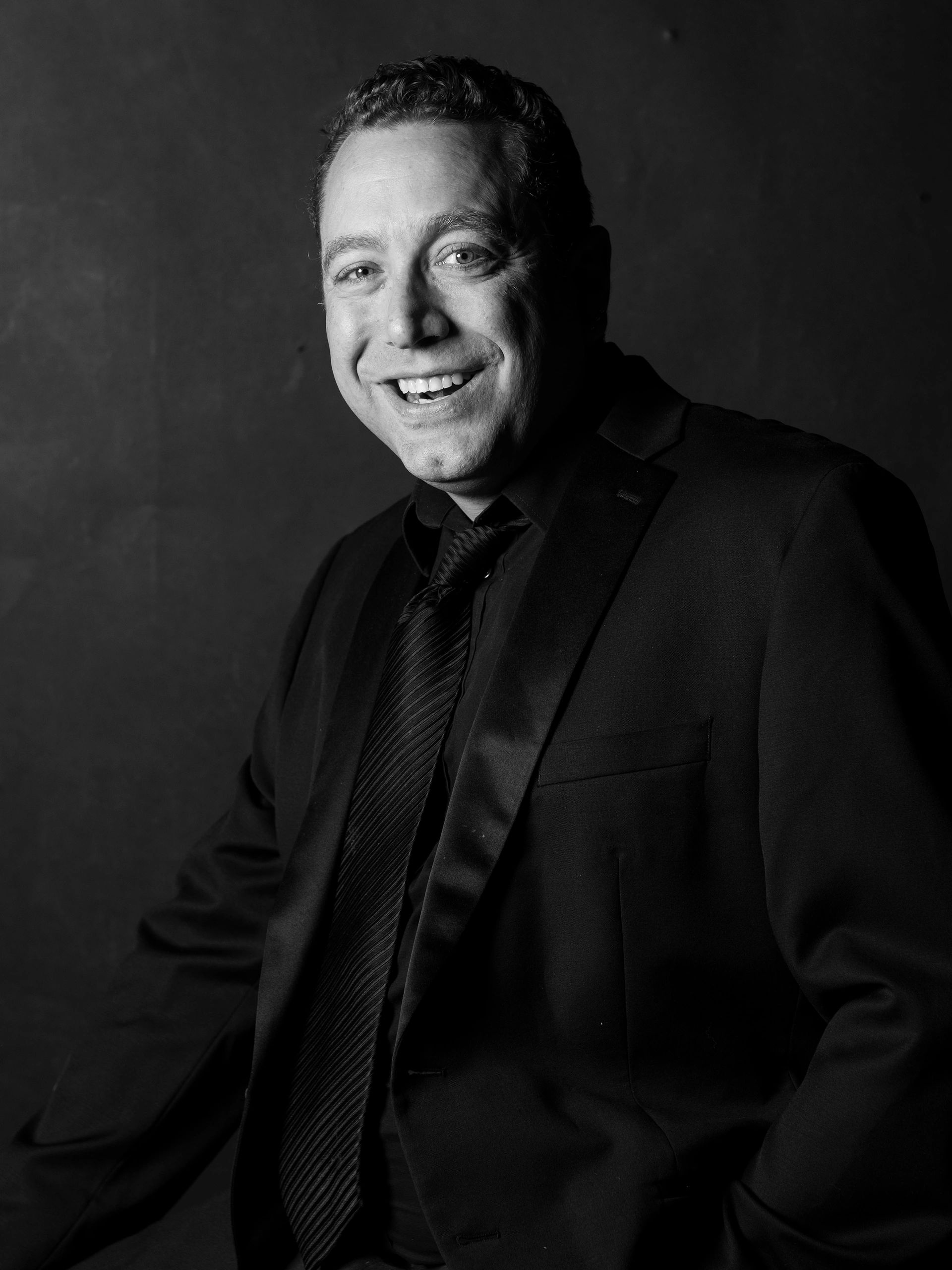 Smiling man in black suit and tie in black and white.