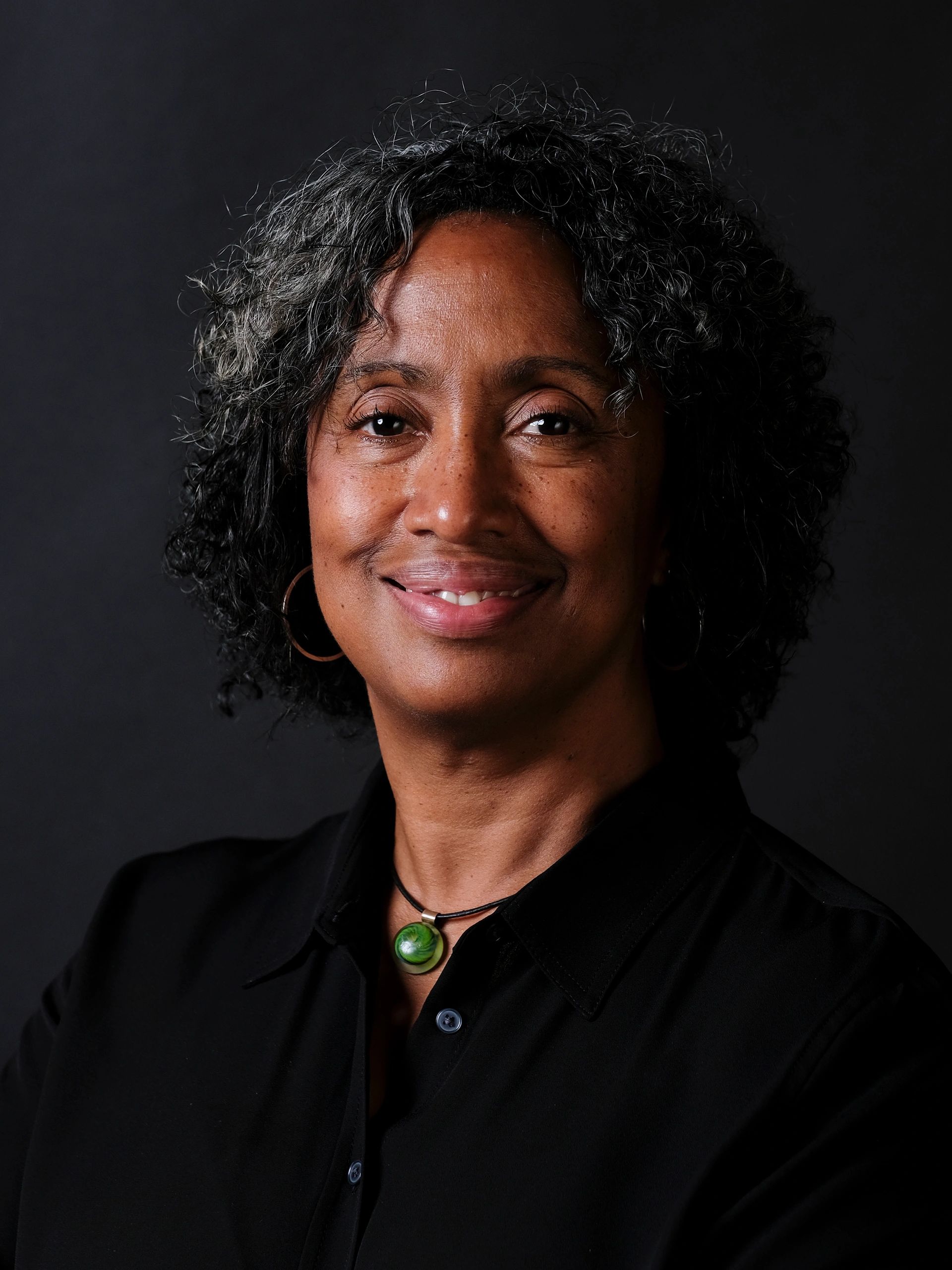 Smiling woman with curly hair and green pendant necklace.