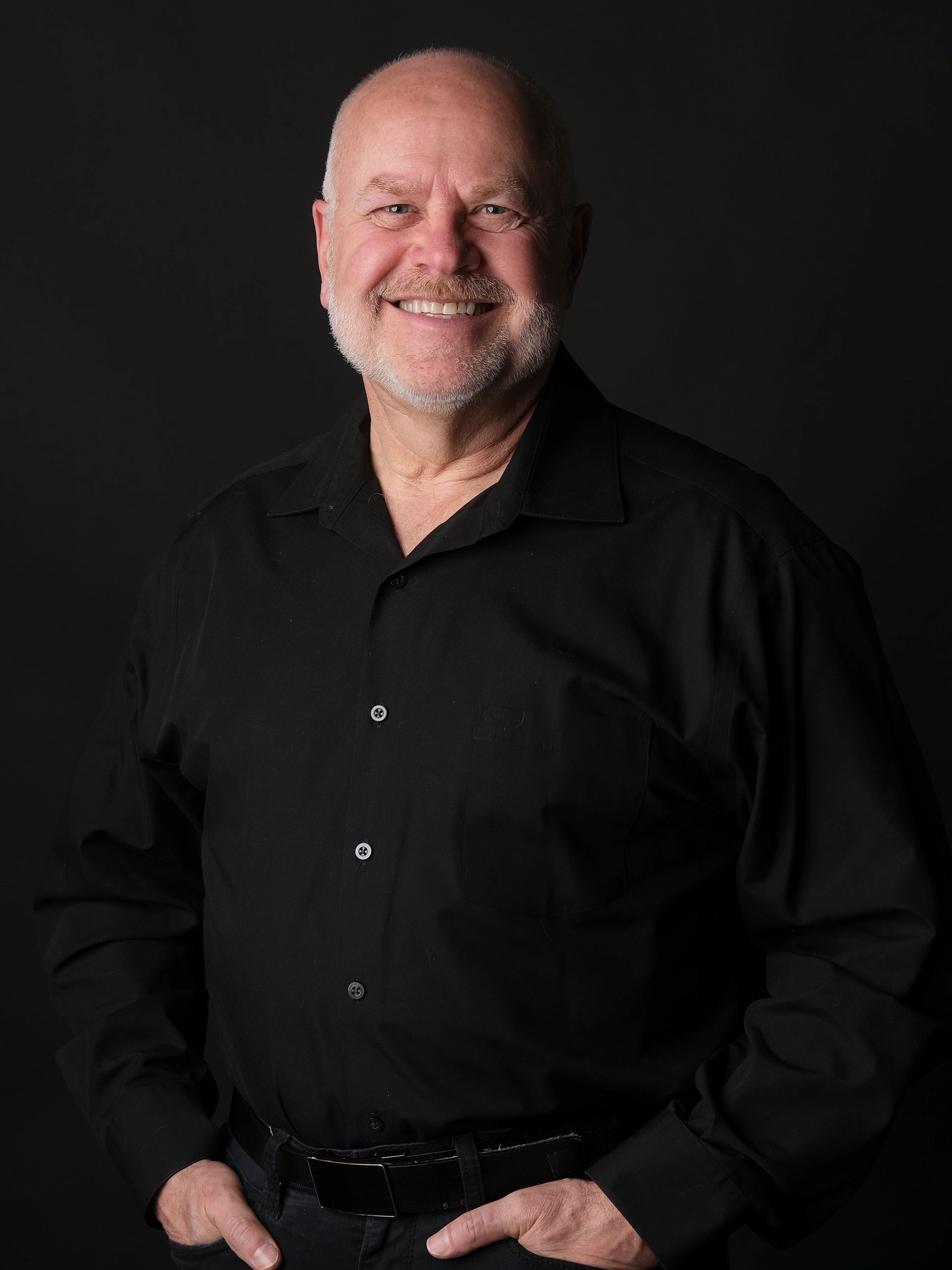 Smiling bald man in black shirt against a dark background.