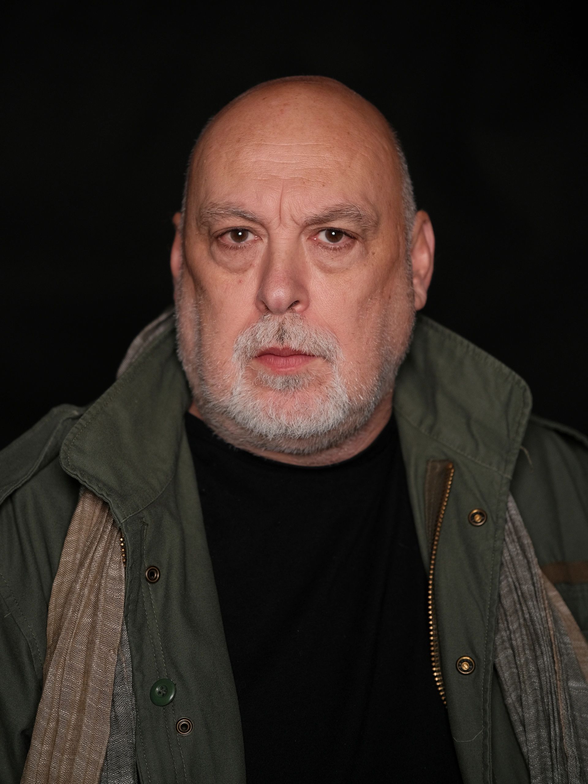Serious older man with a beard against a dark background.