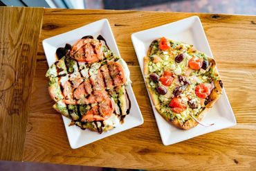 Two gourmet flatbreads with fresh toppings on white plates.