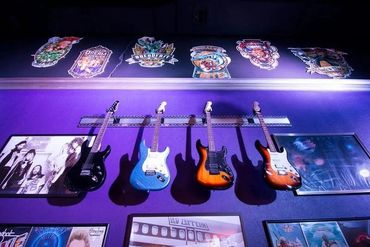Four electric guitars displayed on a purple wall with band photos and logos above.