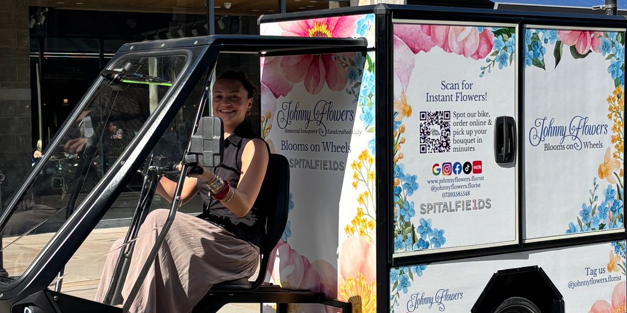 A woman smiles while driving a flower delivery tricycle decorated with floral designs.
