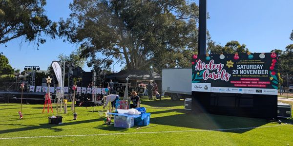 Outdoor setup for Aveley Carols event with stage and decorations on a sunny day.
