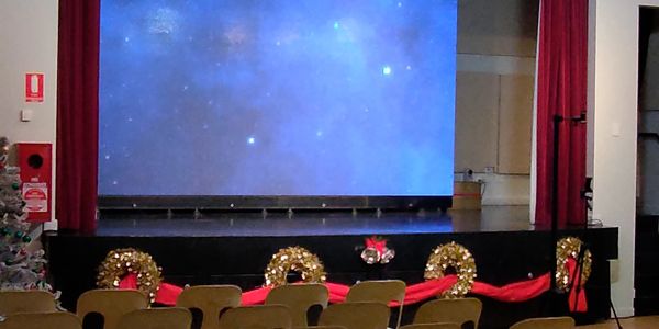 An empty stage with starry backdrop and Christmas decorations in front of chairs.