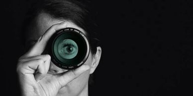 Person holding a camera lens with an eye visible inside it.