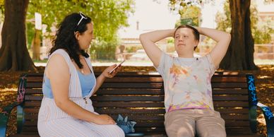 Two people sitting on a park bench, one using a phone.