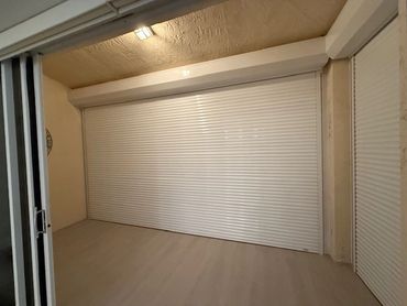 Indoor space with closed white roller shutters and beige walls.
