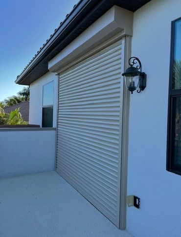 Closed beige rolling shutter on a white exterior wall with a decorative lantern.