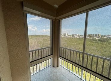 Corner balcony with screened windows overlooking greenery and distant buildings.