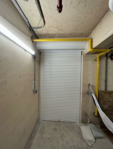 White rolling shutter door in a narrow, industrial hallway with yellow pipes.