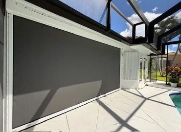 Retractable outdoor shade screen on a poolside patio under a screened enclosure.