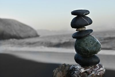 zen rock tower on the beach with waves and a large boulder in the background.