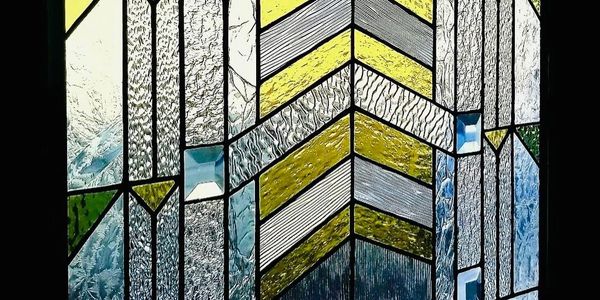 Stained glass window with geometric patterns in yellow, blue, and clear textured glass.