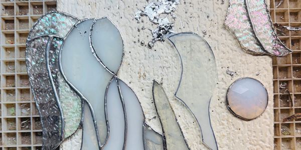 Unfinished stained glass art with iridescent and opaque pieces on a textured board.