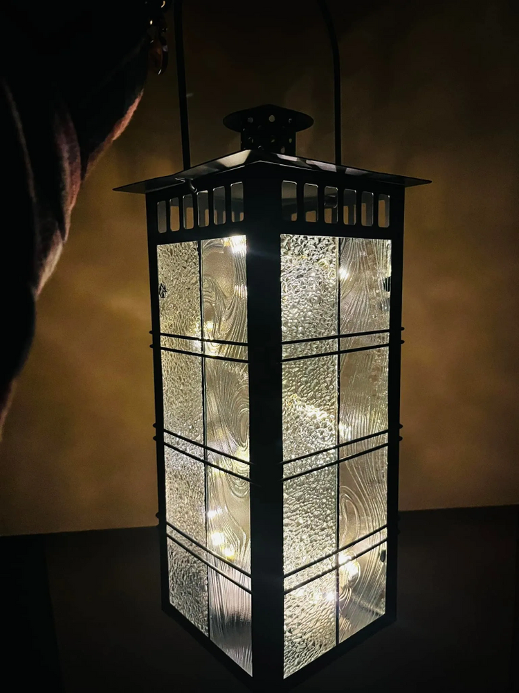 A glowing lantern with textured glass panels illuminating the dark surroundings.