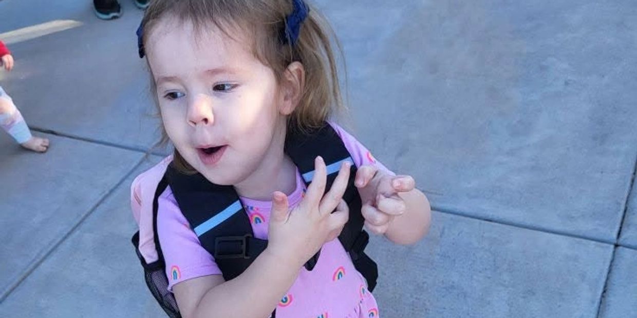 Young girl wearing a pink dress and backpack making a playful face.