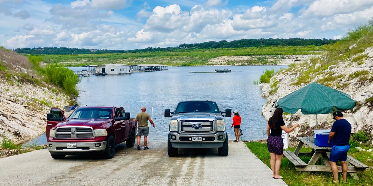 People prepare to launch boats at a lake boat ramp on a sunny day.