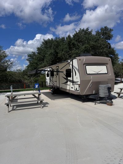 Travel trailer parked on concrete with picnic tables and blue sky.