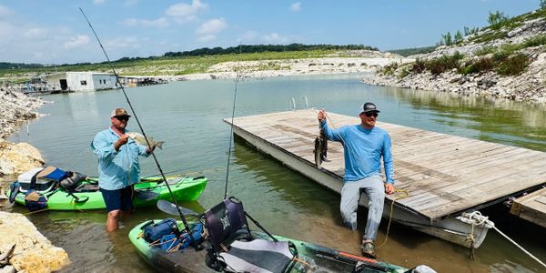 Two men fishing with kayaks by a lakeside dock on a sunny day.