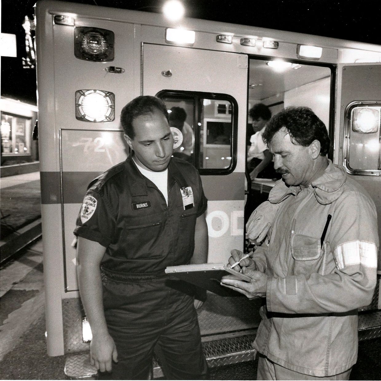 Two emergency responders discussing paperwork near an ambulance.